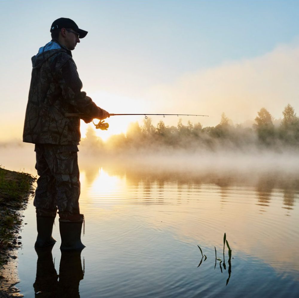 Man fishing in a calm lake at sunrise, surrounded by mist with trees in the background in rathdrum id