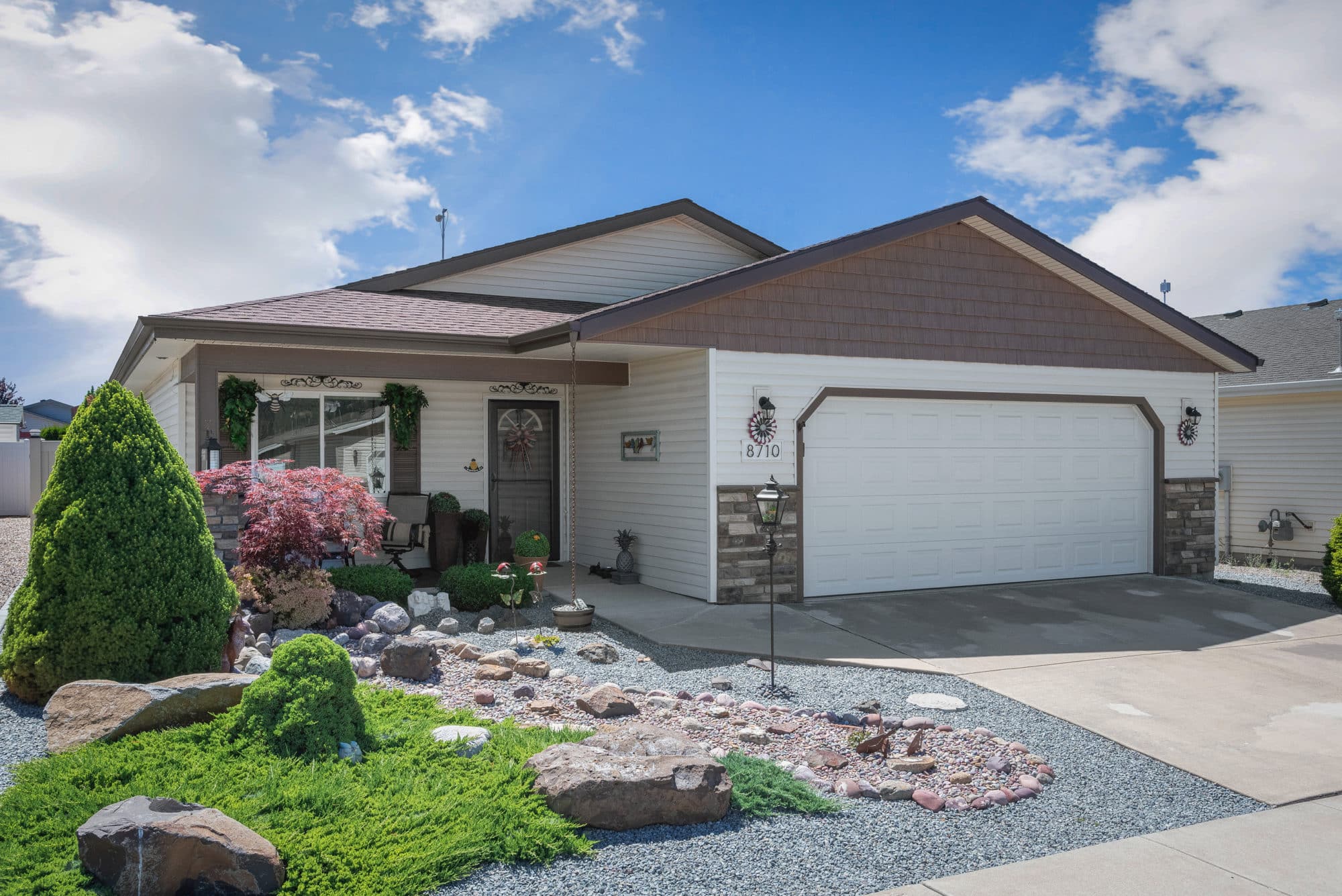 Single-story house with a white exterior, decorative landscaping featuring rocks and shrubs, and a small porch with seating in rathdrum id