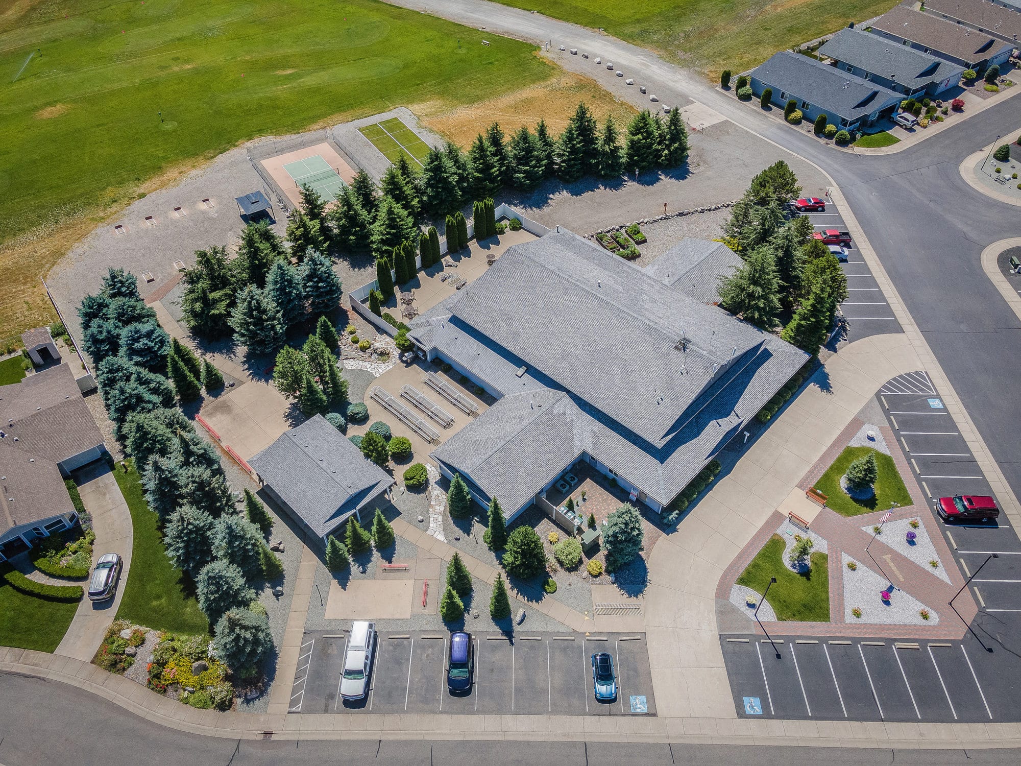 Aerial view of a clubhouse surrounded by parking, tennis courts, and landscaped paths with green areas in rathdrum id