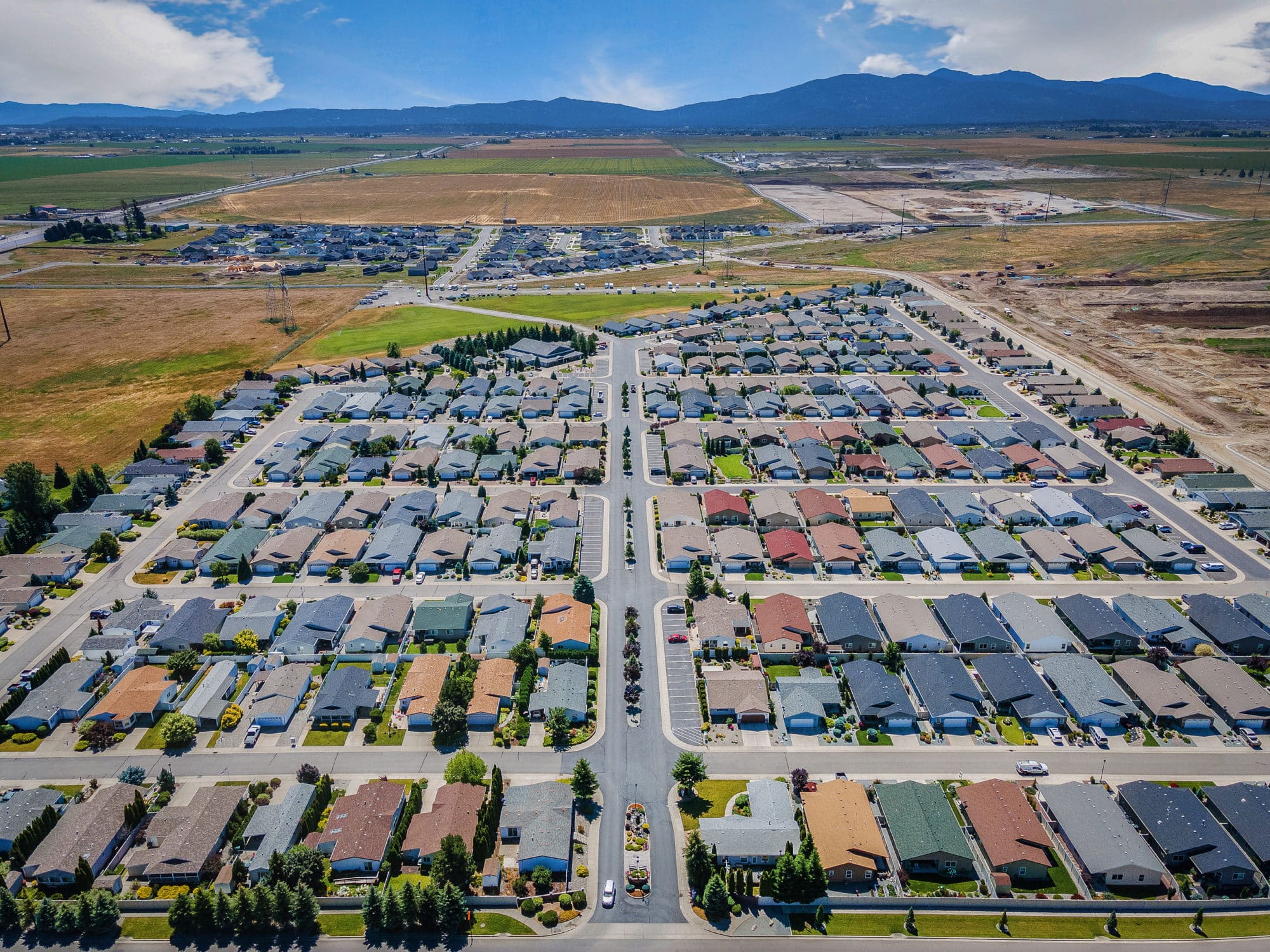 Aerial view of a neatly organized residential neighborhood with rows of houses, surrounded by fields and mountains in the background in rathdrum id