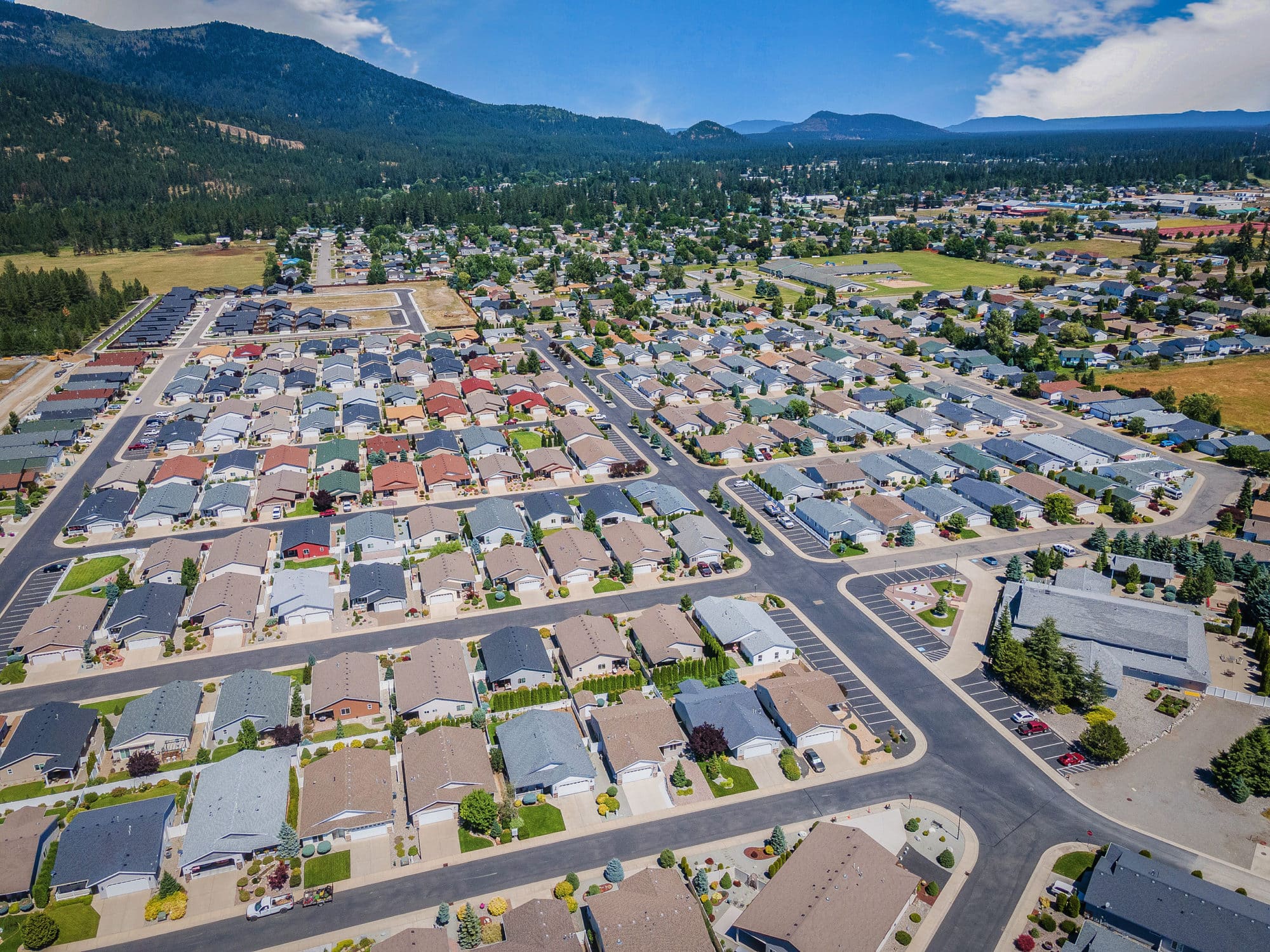Aerial view of a neighborhood with rows of houses and tree-lined streets, surrounded by greenery and mountains in the background in rathdrum id