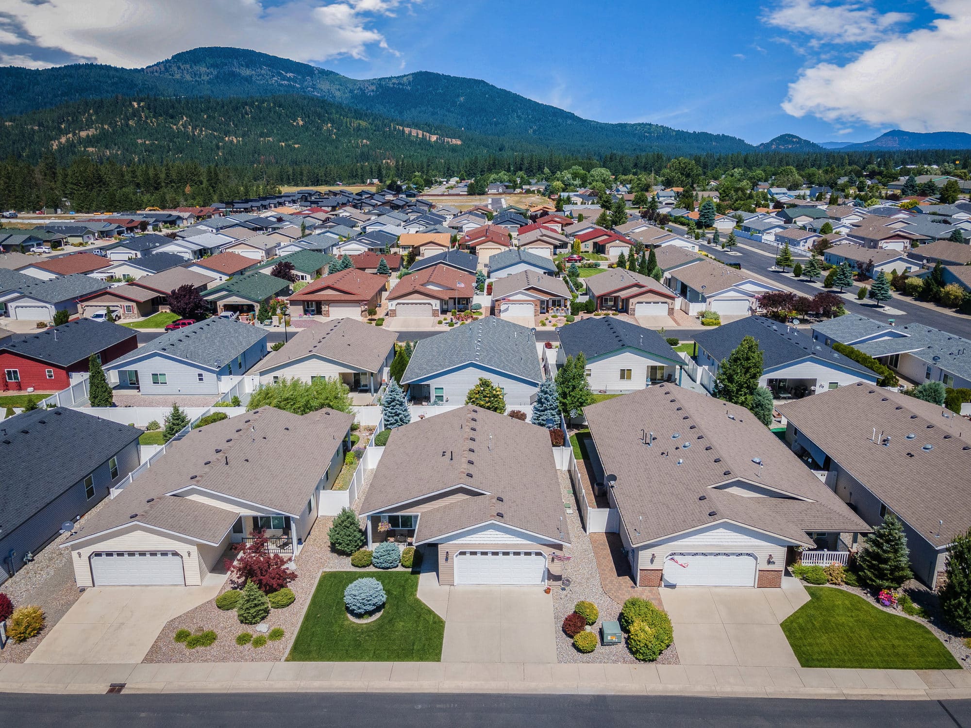 Rows of neat houses with colorful roofs and green lawns, set against a backdrop of forested hills and blue sky in rathdrum id