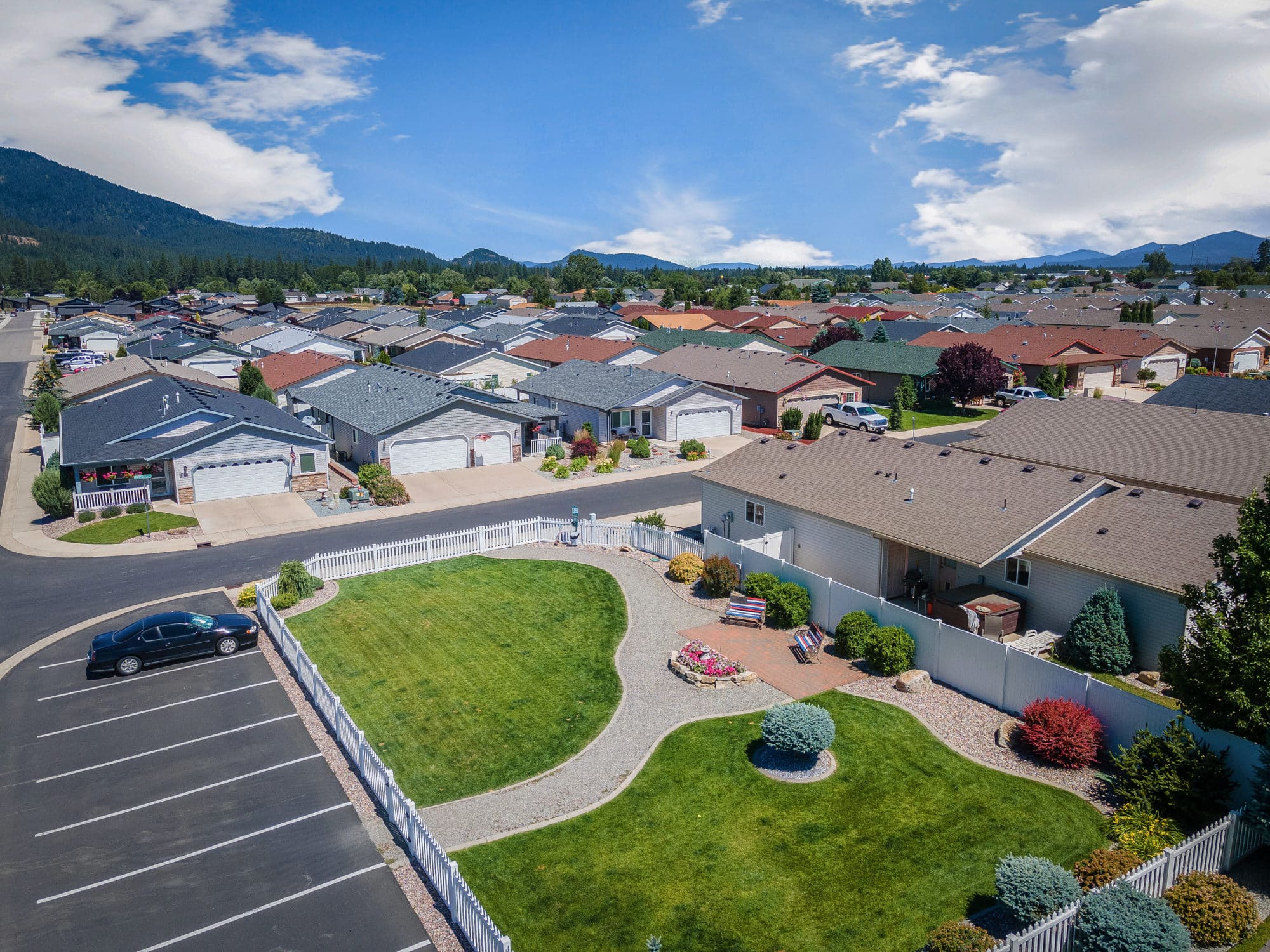 Aerial view of a residential community with houses, a fenced backyard, and a grassy open space with a small garden and seating area in rathdrum id